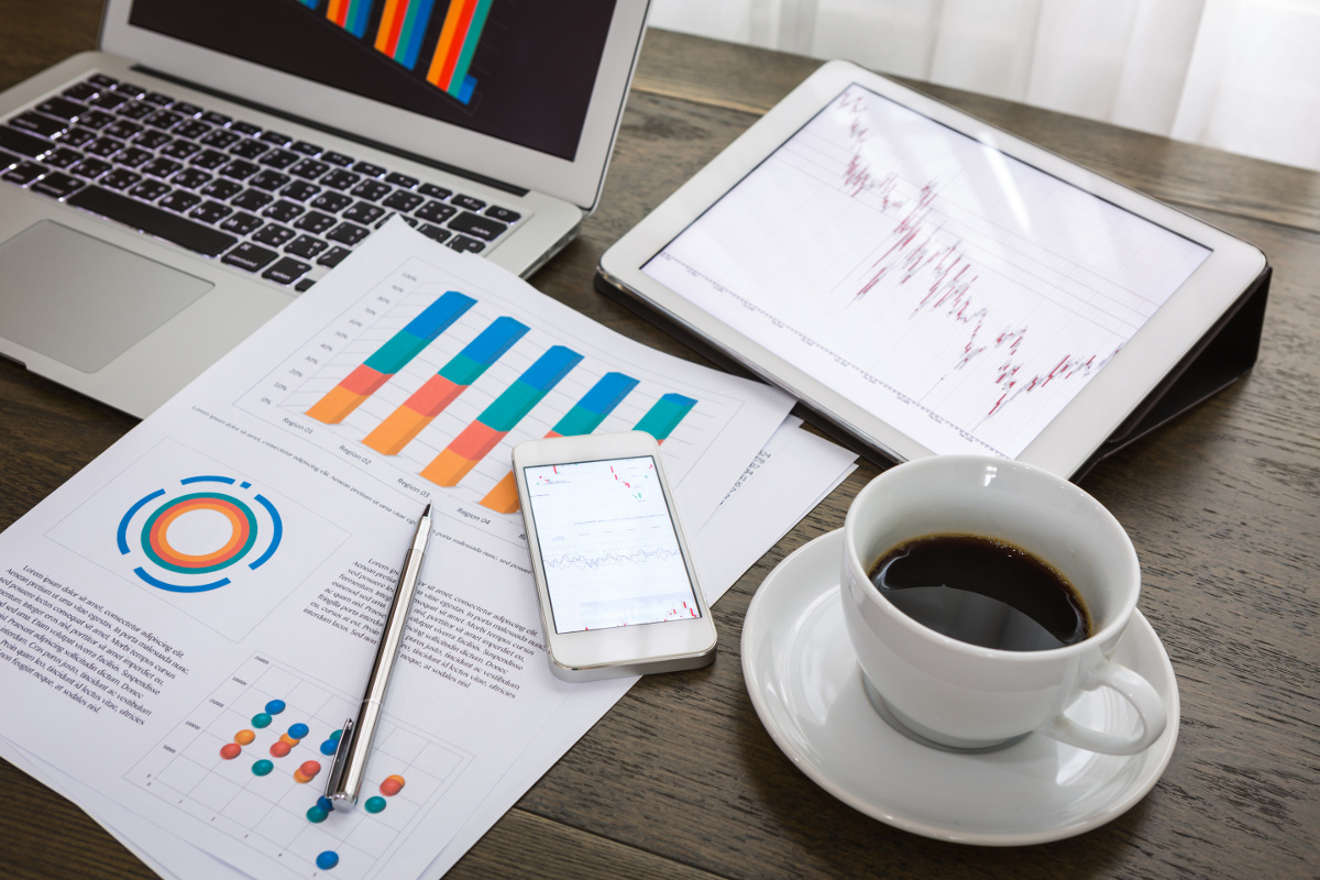 Laptop, Tablet, Cell Phone and Papers on Desk Showing Charts and Graphs