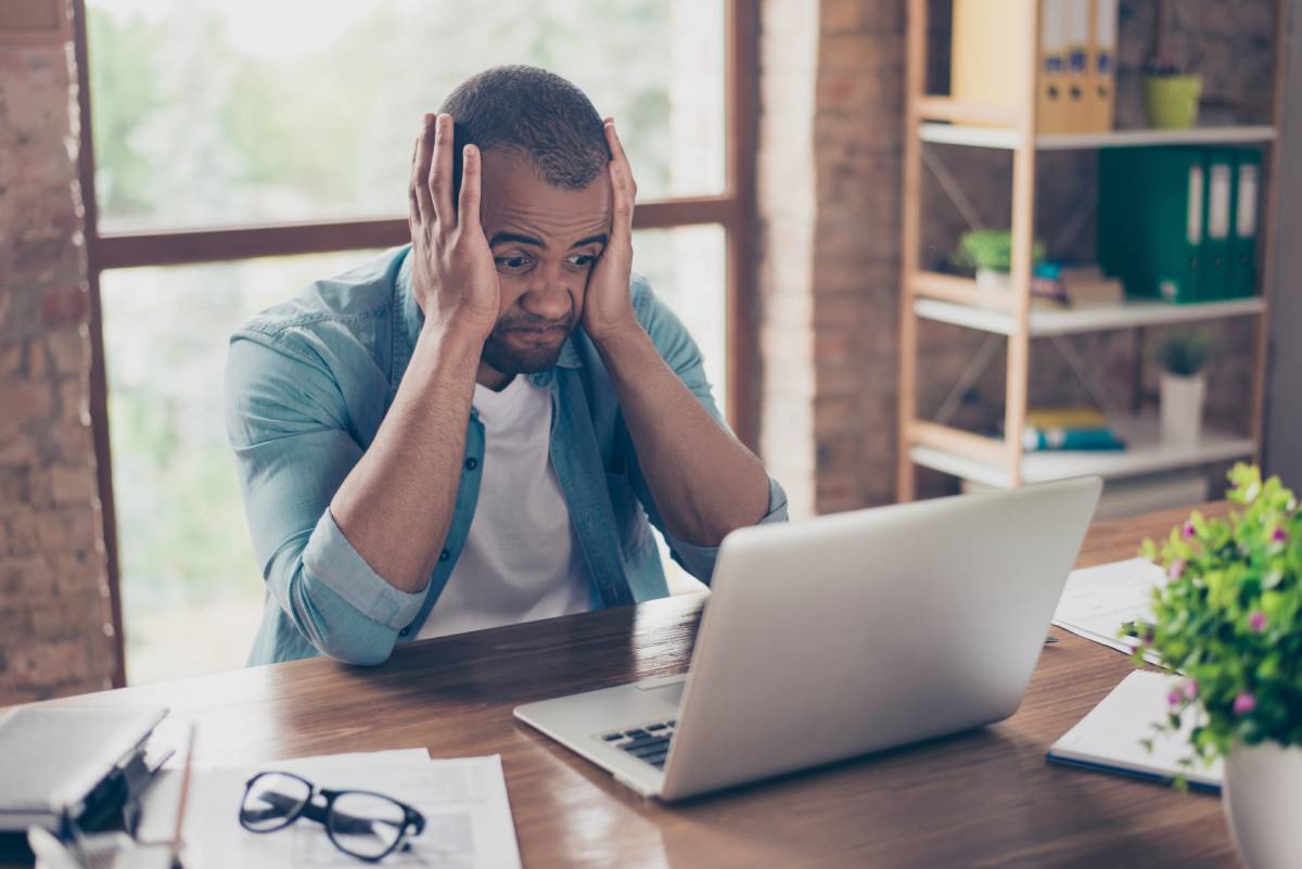 A man with his head in his hands looking at a his computer in frustration