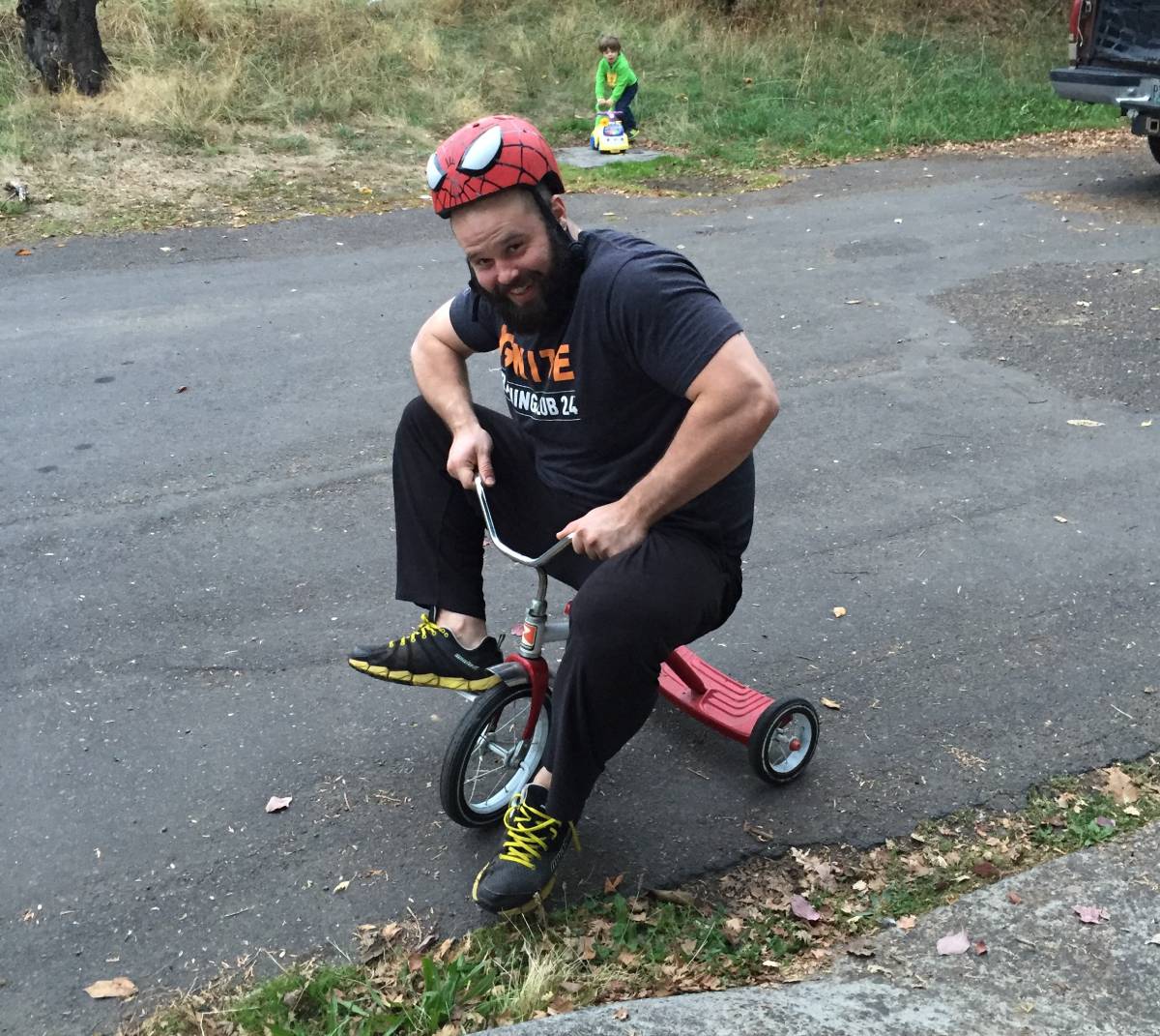 Adam Robinson riding a tricycle wearing his son's Spider-Man helmet