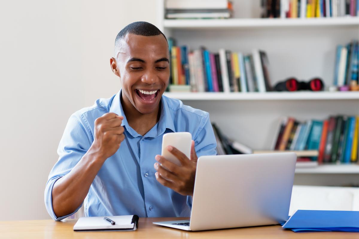 Smiling man looking at his phone while sitting in front of a laptop