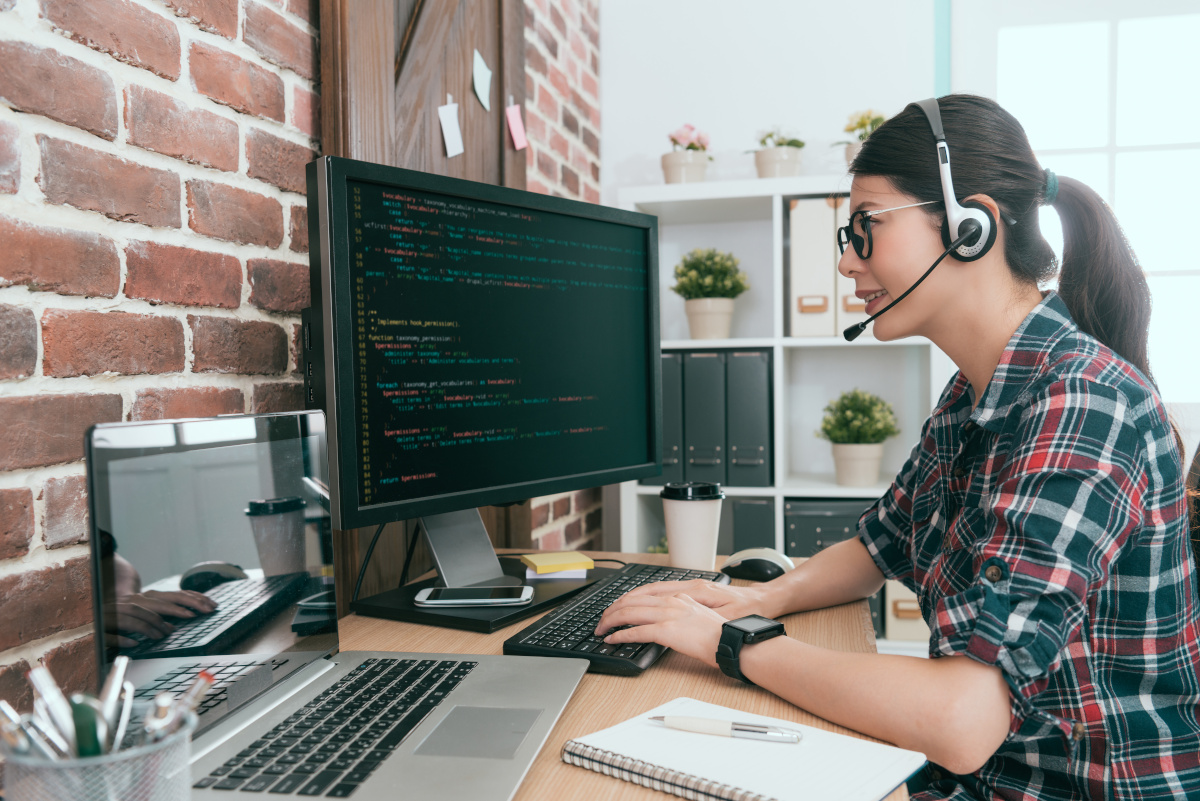 A woman working on her desktop computer while wearing a phone headset in her office at home.