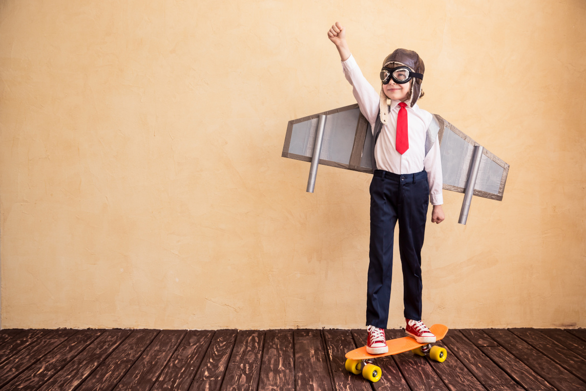 Child dressed up as businessman with cardboard wings. Success, improvement, innovation concept.