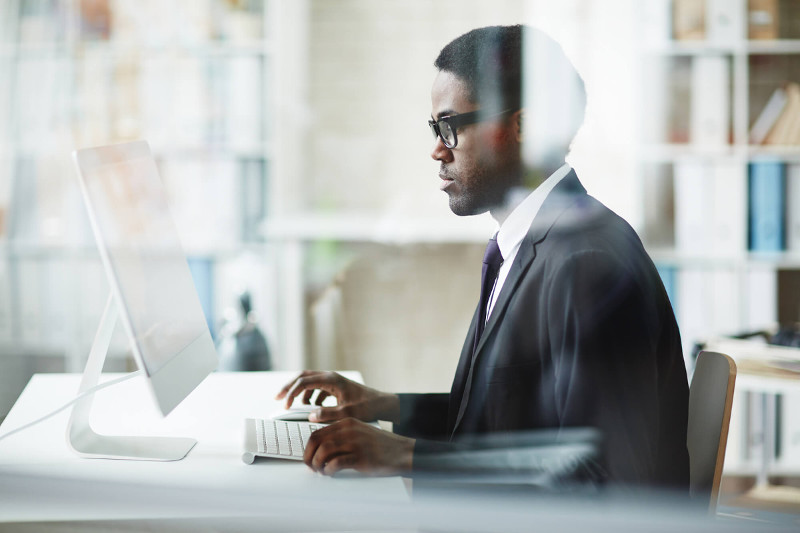 Man wearing glasses using a desktop computer on a white desk